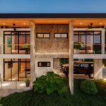 Side facade of a contemporary mountain house with warm textures, concrete walls, a firepit, and LED lighting.